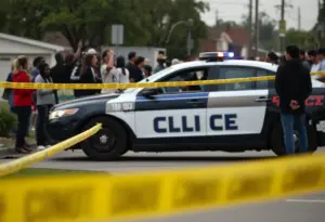 Police car at shooting scene in Laurel County with community members present.